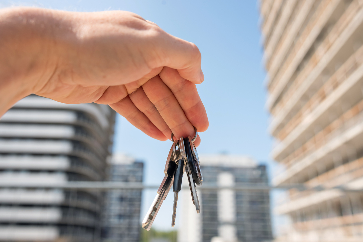 a person holds a key with a house keychain in front of a building under construction
